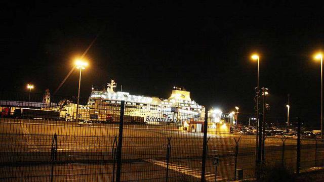 The ferry is about to leave, in the port of Ouistreham. In the foreground, two barriers, migrants, attracted by Britain, want to cross. | Laurent Neveu