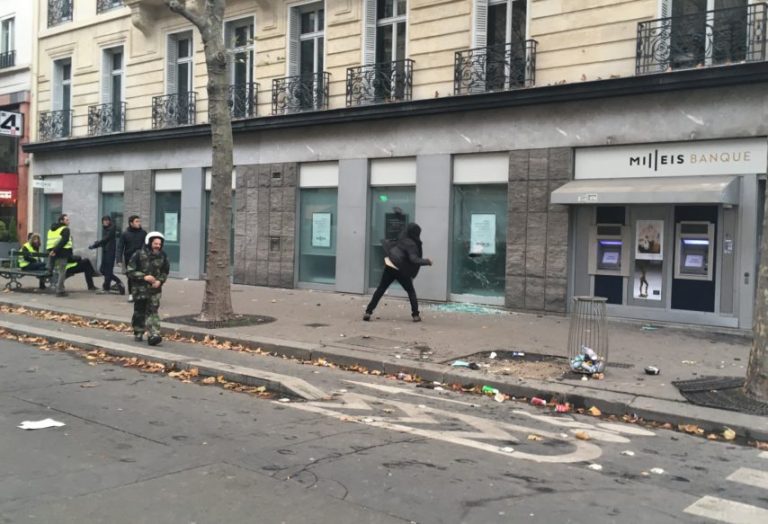 A Protestor throws a pavement in the window of a bank in Paris.