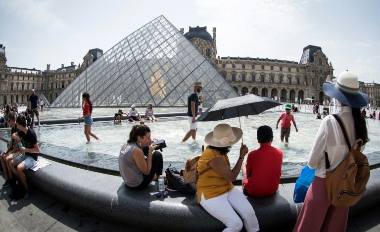 Tourists refreshing themselves at the fountain facing the Louvre pyramid, in Paris on August 7, 2018.