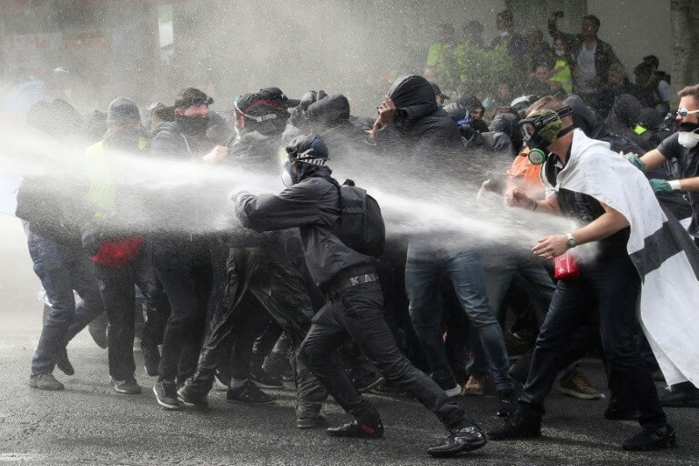 Protesters in black and hooded watered by water cannons during clashes with the police on May 1st, 2019 in Paris.