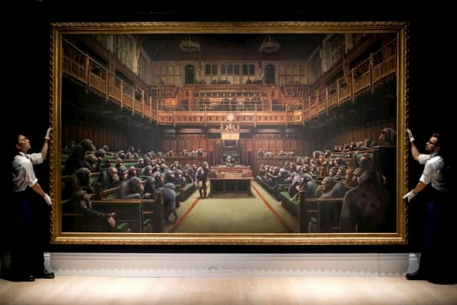 Two assistants manipulate Banksy's "Devolved Parliament" canvas on 27 September 2019 in London.