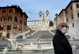 A man wearing a coronavirus mask walks near the deserted Spanish Steps in Rome on March 12, 2020.